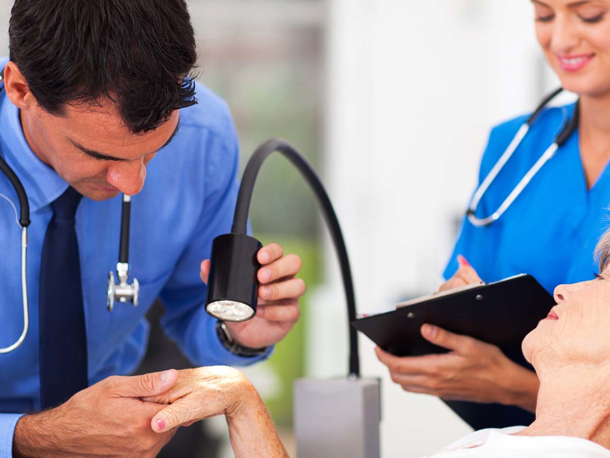 Dermatologist examining a senior woman’s skin under light.