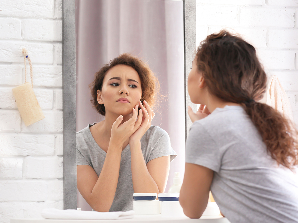 Woman checking her skin in bathroom mirror