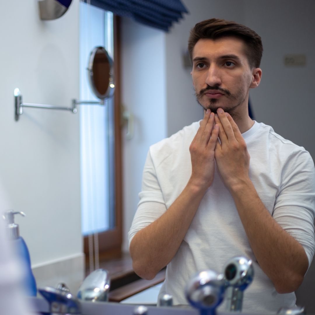 man looking at patchy beard in the mirror