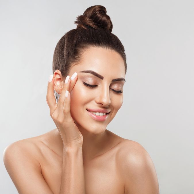 Woman smiling while touching her skin on her face