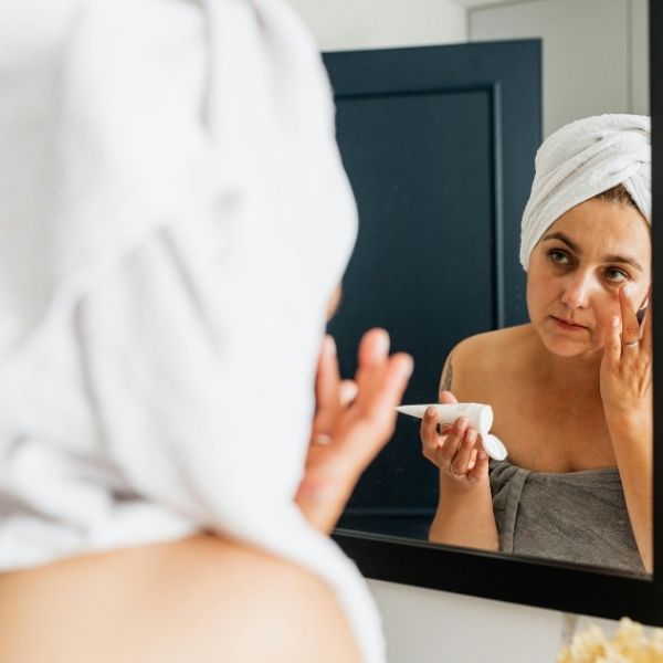 woman in towel applying cream to face