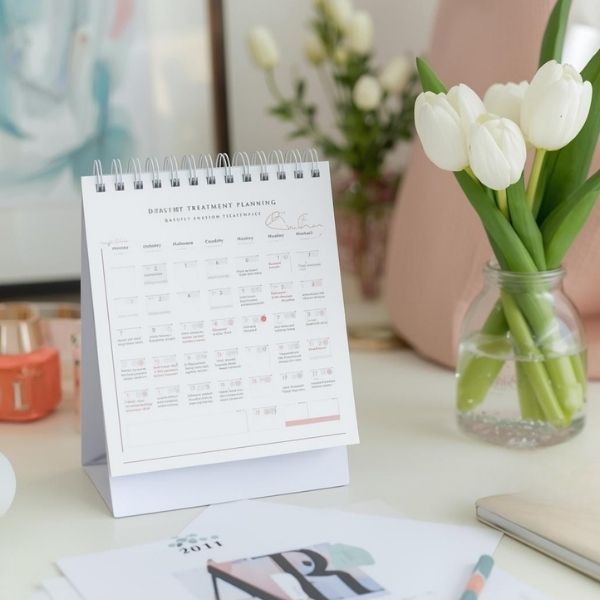 A desktop arrangement with a calendar and a spring flower, symbolizing beauty treatment planning.
